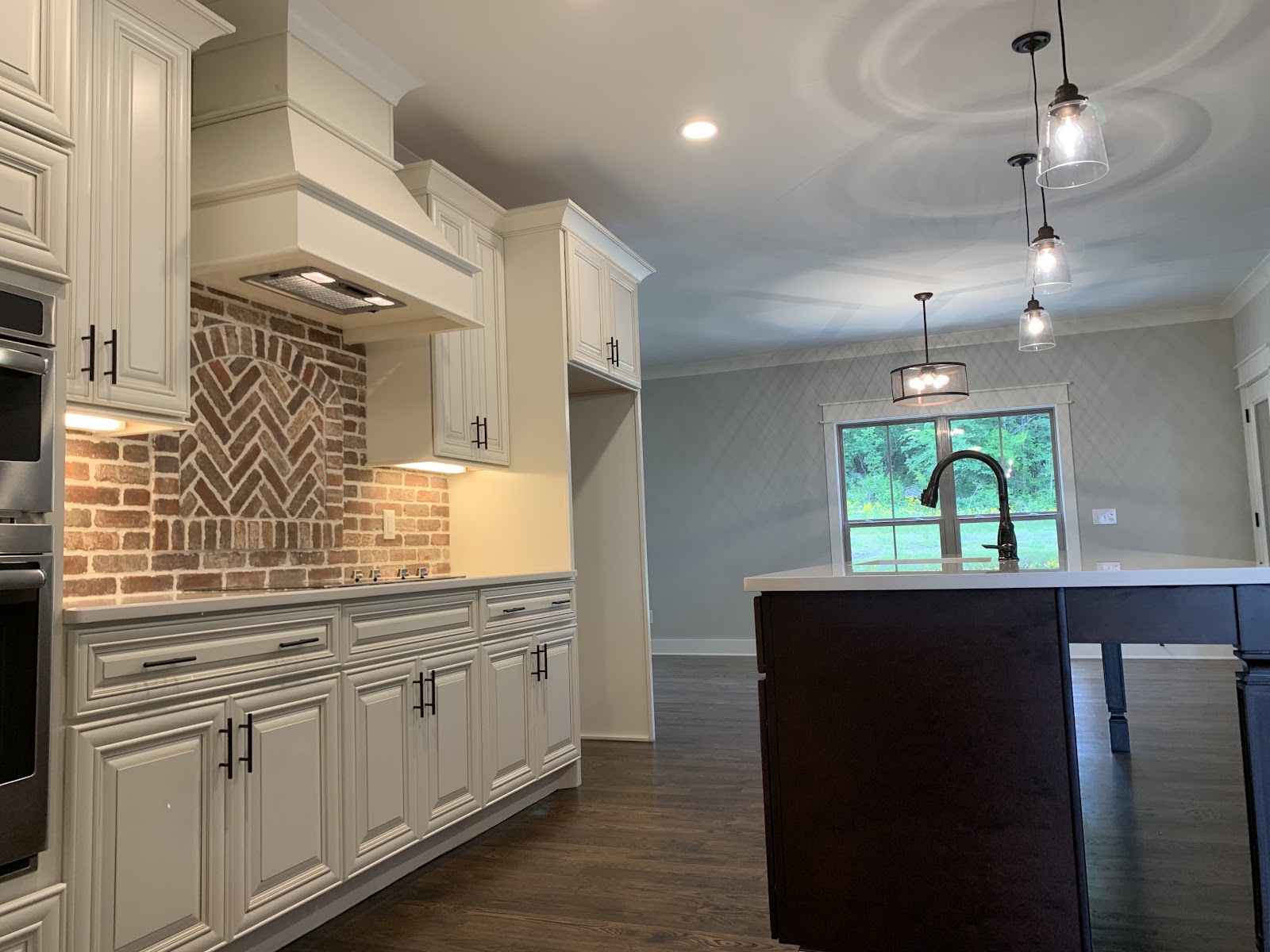 Kitchen featuring white cabinetry, a brick backsplash with a herringbone pattern over the stove, and a dark wood island.