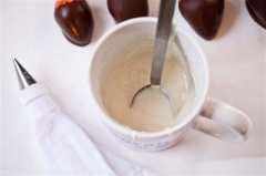 Cho chocolate trắng đã đun chảy vào túi bắt kem. Dùng túi chocolate trắng này vẽ lên thân trái dâu tây các nét giống quả bóng bầu dục.