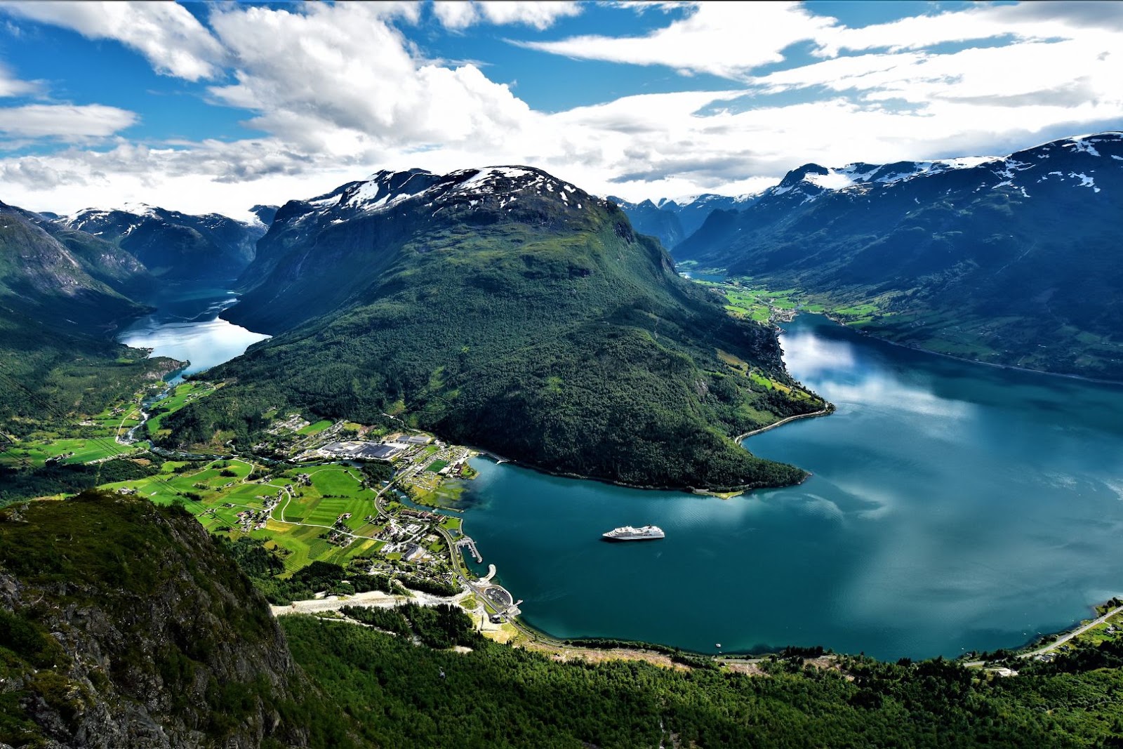 Cruise ship sailing through a narrow Norwegian fjord surrounded by steep green mountains and waterfalls.