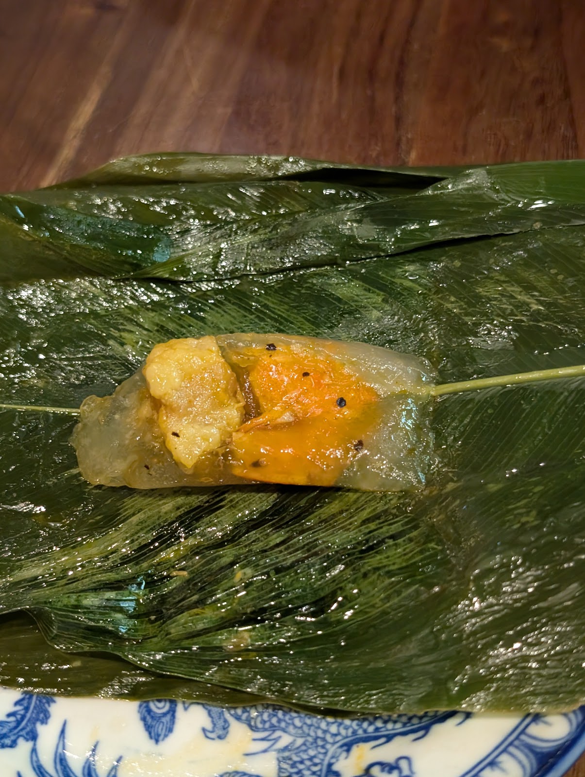 A photo of a banana leaf unwrapped, showing a gooey looking tapioca cake
                 with some chunks of meat inside