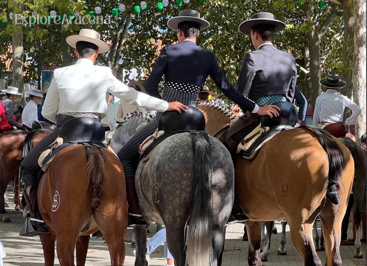Three riders posing on horseback during the Feria de Aracena, photographed from behind.