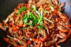 Đổ tôm đã rửa sạch vào, đảo đều. Khi vỏ tôm chuyển màu đỏ đều thì nêm tiếp 8ml rượu, 2g muối, 10g đường, xào tiếp cho tôm ngấm gia vị và cạn nước. Cho hành lá và ngò rí vào đảo đều, tắt bếp.
