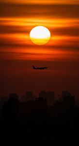High-Contrast Telephoto Silhouette of an Airplane and City Skyline Against a Fiery Orange Sunset