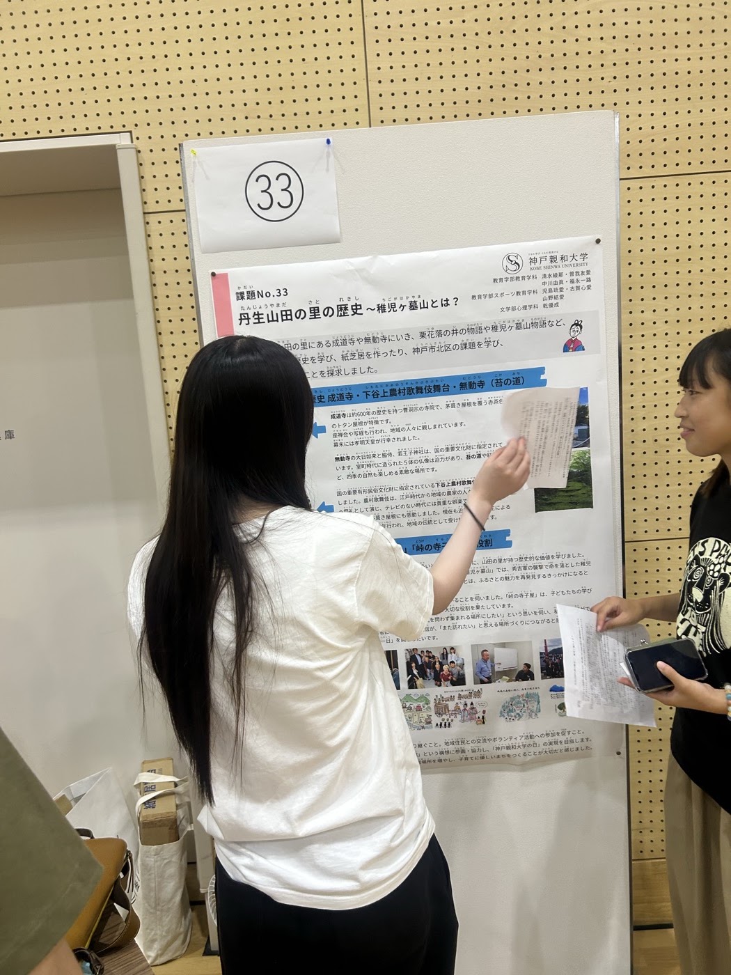 丹生山田の里の歴史をまとめたポスターの前で説明する学生