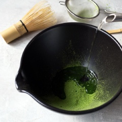 Đầu tiên, rây bột matcha vào tô, cho tiếp 1/4 chén nước nóng vào cùng. Hãy để cho bột matcha nở ra trong khoảng 1-2 phút, khuấy nhanh để tránh vón cục. Để làm được, bạn có thể sẽ phải dùng đến cây đánh matcha bằng gỗ hoặc cây đánh trứng bằng kim loại loại nhỏ nhé!
