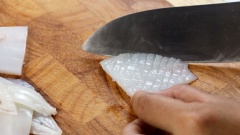 500gr mực ống lột bỏ lớp da bên ngoài, sau đó xẻ mực ra làm đôi. Bóp mực với 5gr gừng băm nhuyễn và 80ml rượu trắng để khử bớt mùi tanh, sau đó rửa lại mực với nước sạch. Thấm khô mực rồi cắt ra thành những miếng nhỏ, sau đó khứa thân mực thành hình vảy rồng (khứa ca rô xéo). Cho mực ra tô, thêm 1 muỗng canh đường rồi bóp nhẹ nhàng từ 3 - 5 phút cho đến khi mực ra nhiều bọt thì đem đi rửa lại với nước sạch.