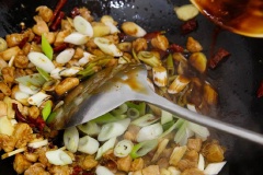 Sau đó đẩy thịt ra phía cạnh, khoảng trống ở giữa cho ớt khô, tiêu vào phi thơm rồi thêm tỏi, gừng, 1/2 hành lá băm vào xào đều. Phần hành còn lại cho vào cùng rồi chế phần nước sốt vào đảo đều cho thịt gà thấm phần sốt. Cuối cùng thêm đậu phộng rang vào đảo một chút để đậu được áo lớp sốt là xong nha. Cho thịt gà ra dĩa và thưởng thức cùng cơm nóng thôi nè.