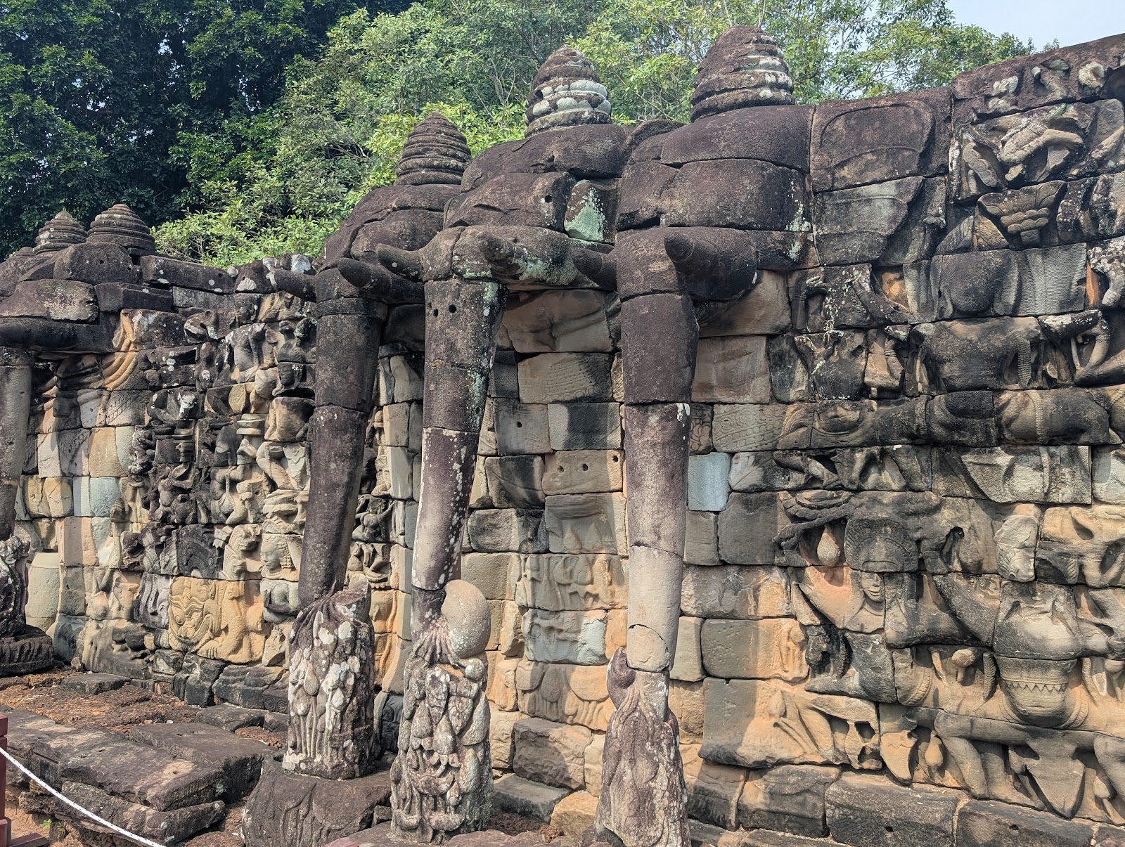 An intricately-carved wall of stone, partially depicting
                 three eleohants heads at the top of the wall with little
                 hats and trunks reaching out and down to the stone tiles
                 below