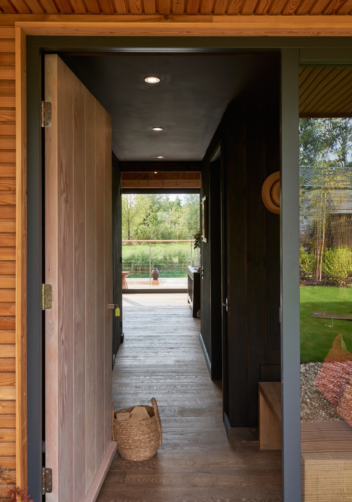 A Cotswold cabin terrace at dusk, garden lights and an open glass-walled living room looking onto the lake