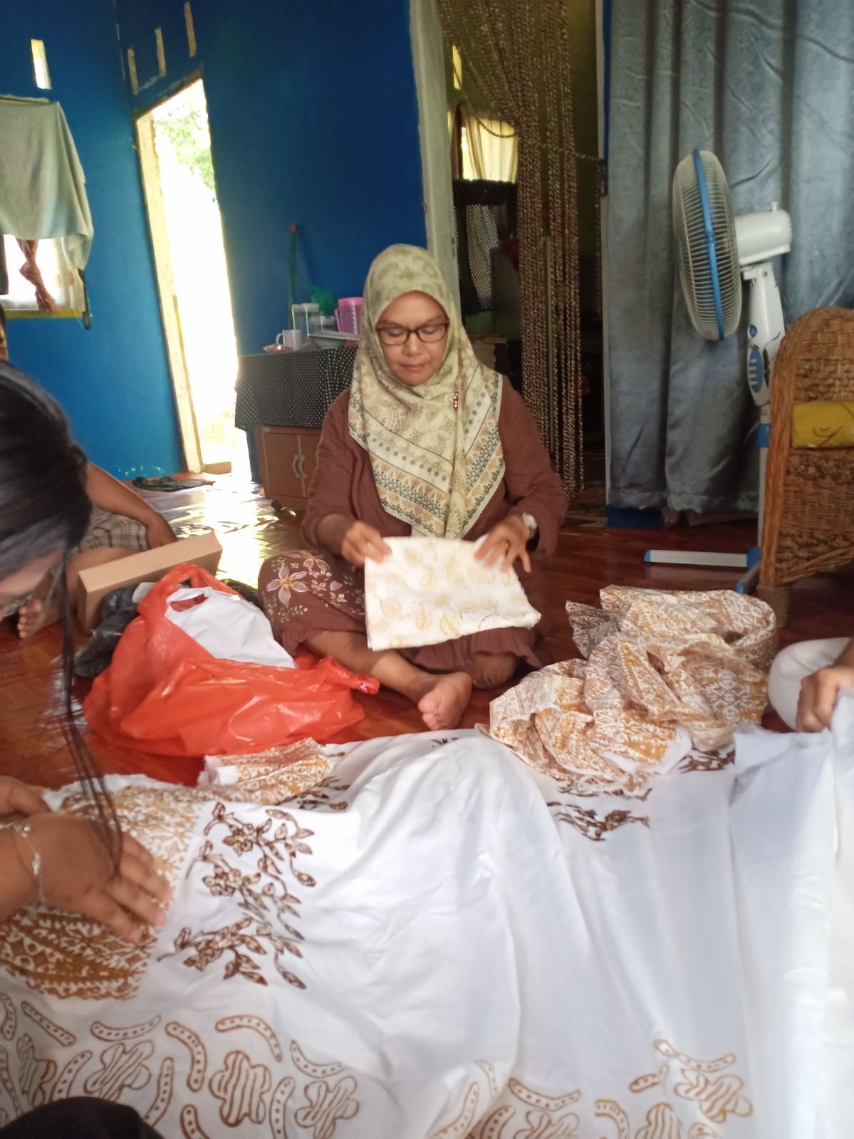 Local Community Ibu Folding Batik with a student drawing mangrove batik on the cloth