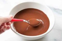 Đun chảy chocolate chips trong 30 giây ở lò vi sóng, nếu chocolate vẫn còn cứng, bạn trộn đều rồi tiếp tục cho vào lò trong 5-10 giây nữa. Cho nước cốt dừa đặc vào chocolate rồi trộn đều bằng tay.