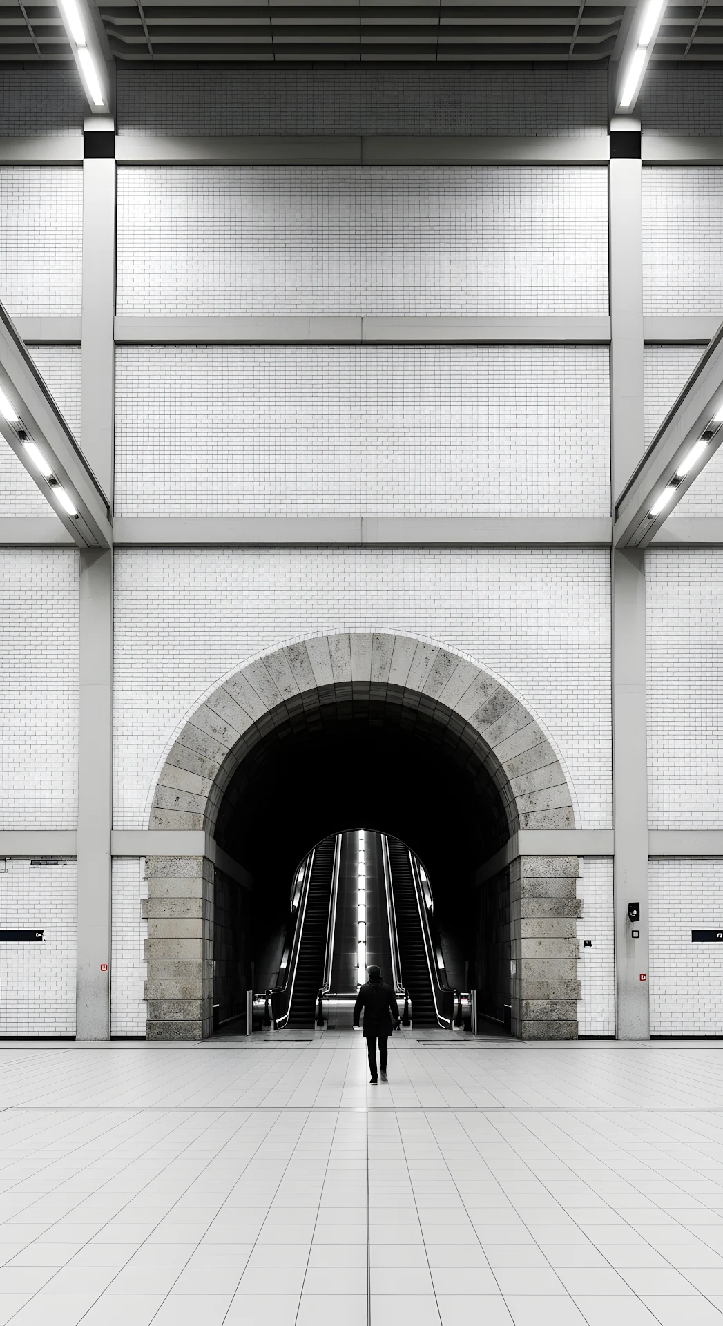 Symmetrical View of a Person Walking Under a Stone Archway in a Modern Underground Station - Free 4K mobile Wallpaper