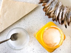 Dùng bột bắp pha với 1/2 chén nước để làm "keo" kết dính dán chắt vỏ bánh. Trải miếng bánh pía lên bàn, để theo hình tam giác. Cho 1 con tôm lên trên bánh pía. Phần đuôi quay ra bên ngoài. Quấn tròn đến 1/2 vòng bánh rồi gập đầu lại.
