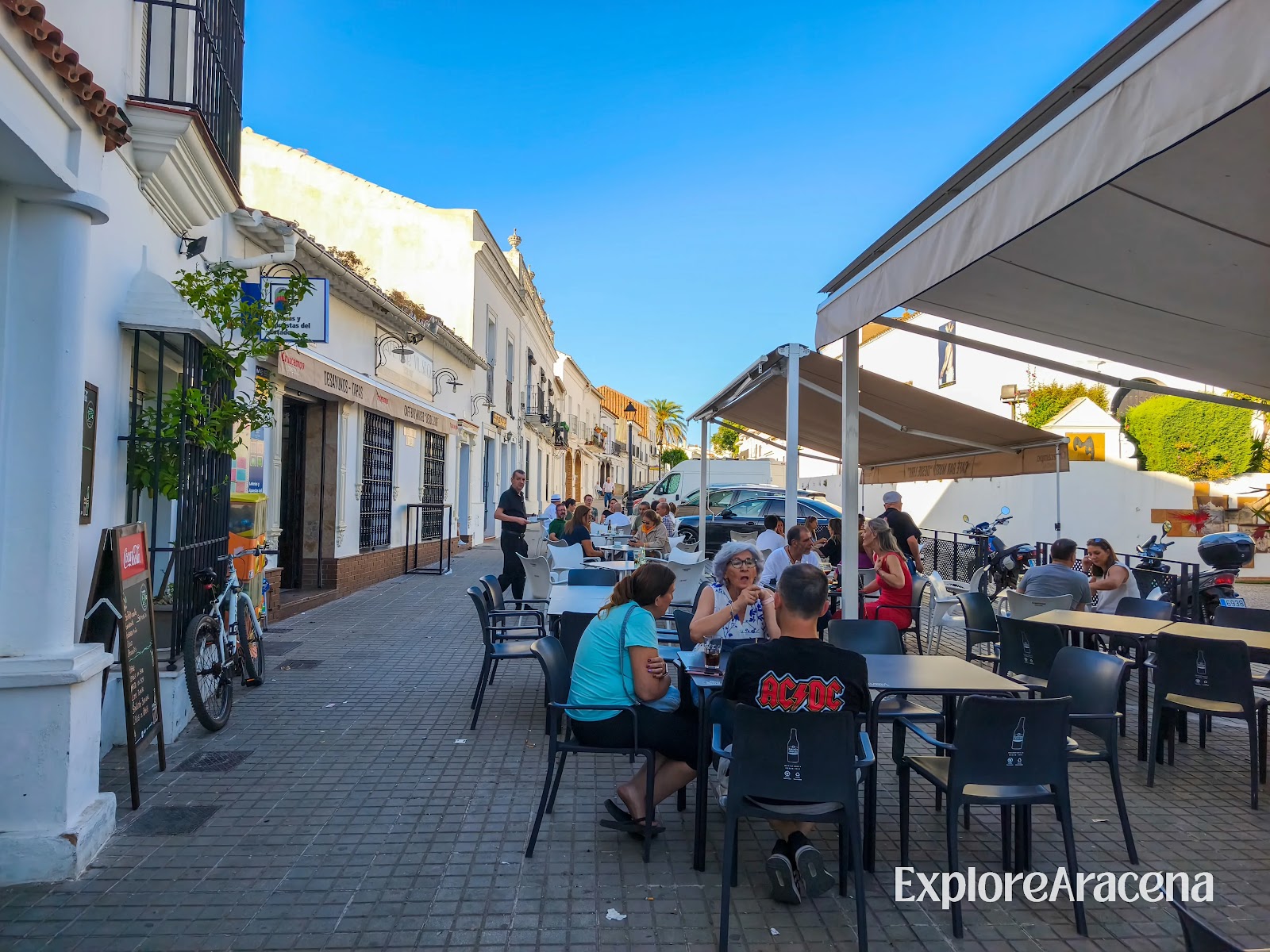 People sitting at outdoor tables in Aracena, sharing drinks and conversation shortly before sunset.