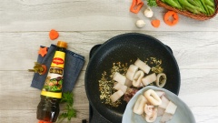 Bắc chảo nóng, phi thơm 10gr tỏi băm với 2 muỗng canh dầu ăn. Tiếp theo cho mực vào xào đến khi săn lại thì cho cà rốt và đậu hà lan vào xào cùng. Nêm 1 muỗng canh hạt nêm và 1 muỗng canh dầu hào giúp món ăn đậm vị hơn.