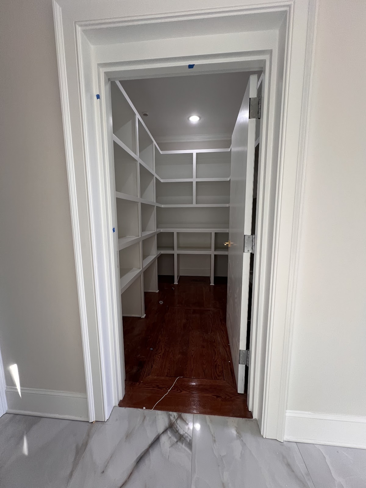 Finished interior of a small room with white built-in shelving and wood flooring, viewed through an open doorway.