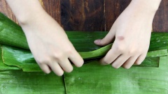 Lá dùng để gói là lá chuối đã được rửa sạch và trụng qua nước sôi giúp chả bò không bị gãy khi gói. Bạn quết 1 lớp dầu ăn bên ngoài lá chuối rồi đặt thịt vào giữa lá và cuốn trước lớp trong cho thật chặt tay rồi mới cuốn lớp ngoài nhé.