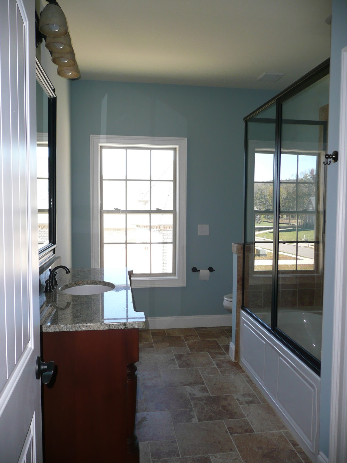 Bathroom interior with blue walls, a dark wood vanity, stone countertop, tiled flooring, and a glass-enclosed shower area.