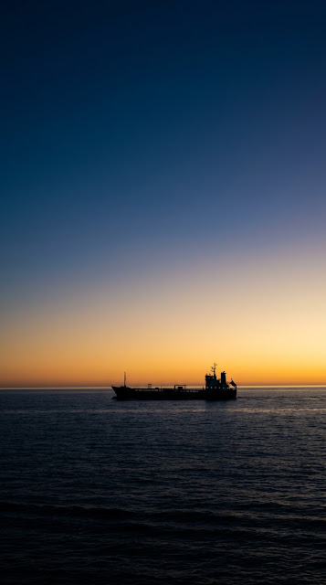 Silhouetted Ship Sailing on Vast Ocean Under Indigo and Gold Sky - Free mobile Wallpaper