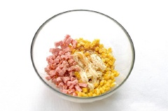 Cho bắp ngọt vào bát, thêm xúc xích, sốt mayonnaise, mật ong, muối và hạt tiêu vào trộn đều. Cho bắp đã trộn vào chảo hoặc khay nướng sau đó rắc đều phô mai lên trên. Làm nóng lò nướng ở 190 độ C, cho khay nướng vào nướng trong khoảng 5 phút hoặc cho đến khi bánh chuyển vàng là được. Lấy bánh ra rắc chút rau mùi tây lên trên là xong.