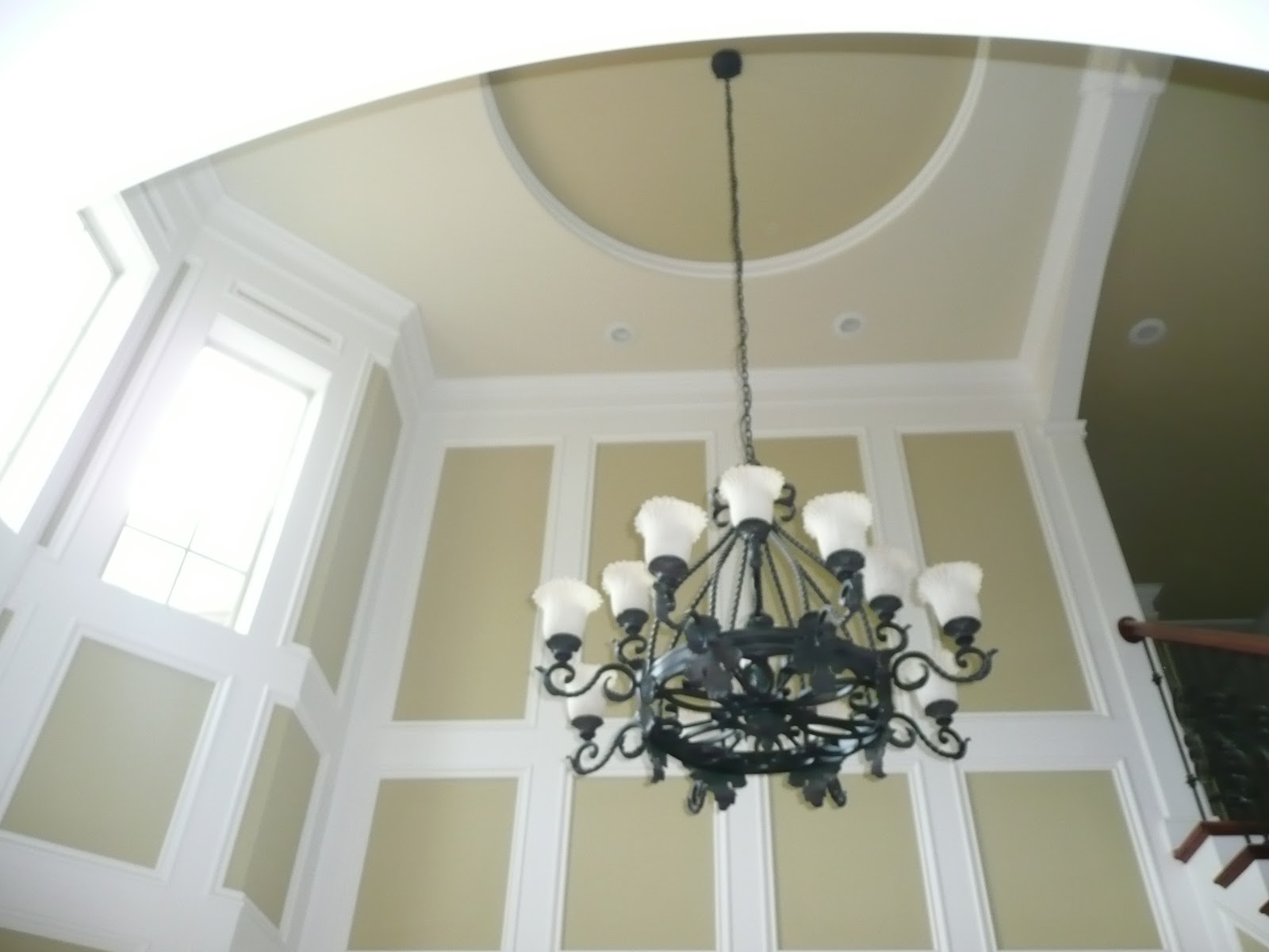 An ornate black chandelier hanging in a room with high ceilings and walls decorated with white trim molding.