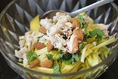 Cuối cùng, cho xoài chín, thịt cua, húng lũi rửa sạch, 1 muỗng canh nước mắm, 1 muỗng cà phê ớt băm, hạnh nhân giã hơi nhỏ vào tô lớn, trộn đều.