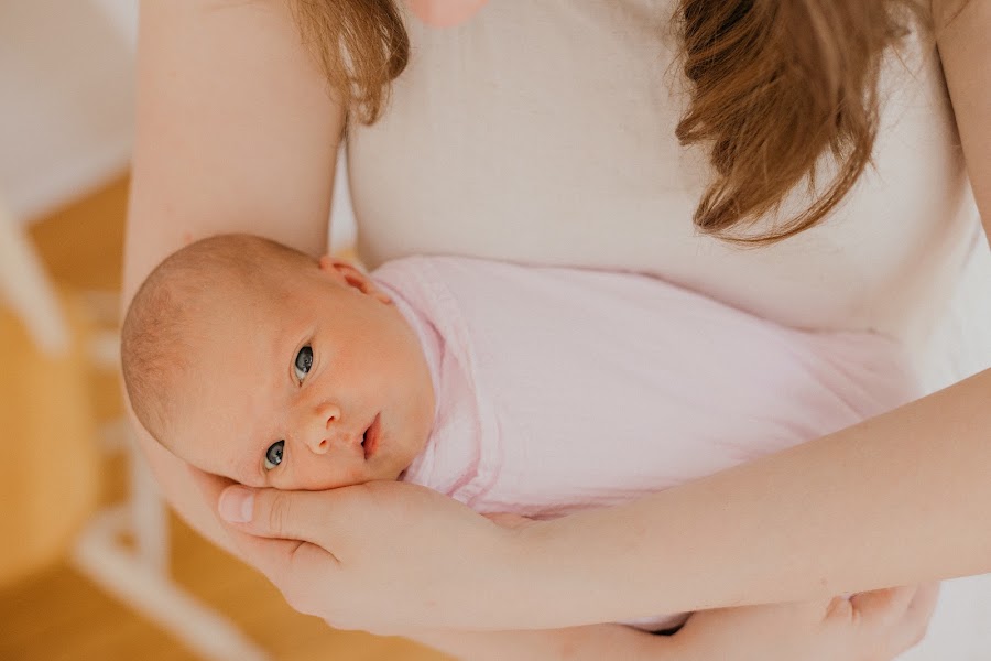 Mother holding wrapped newborn by the window — lifestyle newborn session