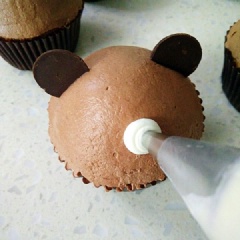 Trang trí + tạo hình bánh cupcake chocolate đẹp mắt: Cho hỗn hợp chocolate vào túi bóp kem, bắt kem hình chóp lên những chiếc bánh. Tiến hành trang trí bánh thành hình những mặt gấu đáng yêu nữa là hoàn tất.