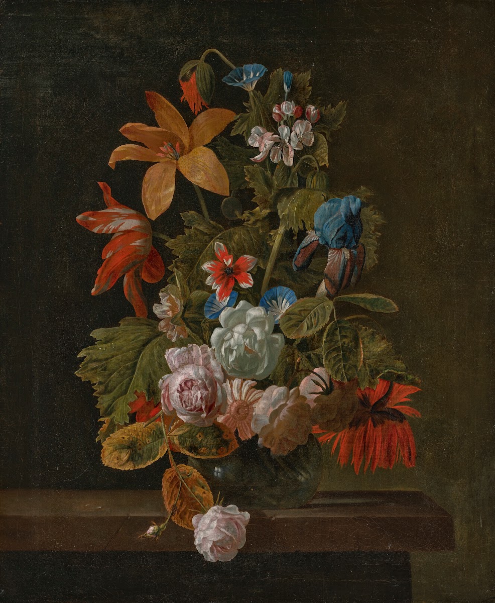 Tulips roses an iris and various flowers in a glass vase on a stone ledge