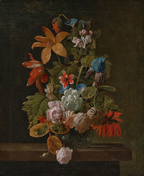 Tulips roses an iris and various flowers in a glass vase on a stone ledge