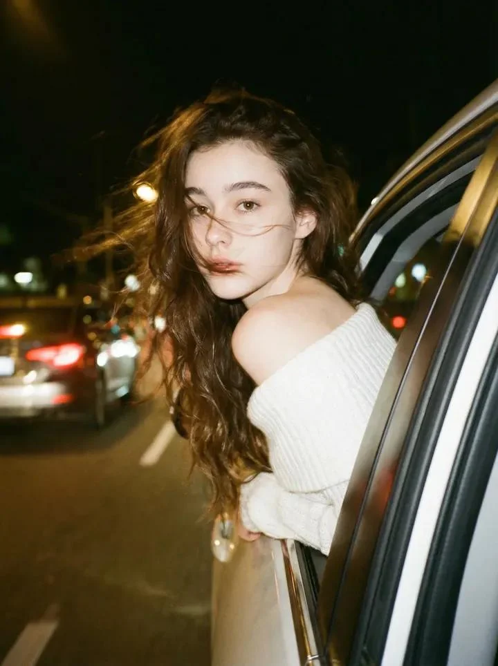 Foto mía asomada por la ventanilla del coche en una noche oscura y onírica de estilo vintage.