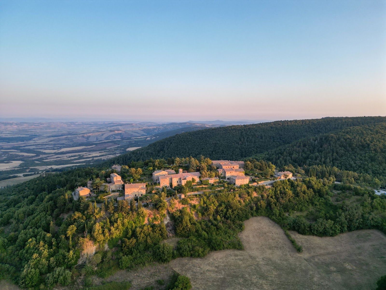 An aerial view of a small Tuscan hill village on a wooded ridge above open countryside