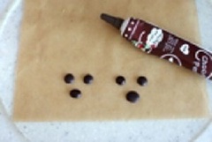 Sau đó chúng mình tạo các hạt tròn nhỏ bằng chocolate để làm mắt gấu nhé. Khi nào các hạt sô cô la này khô thì đặt nhẹ nhàng lên phía trên ly bánh.