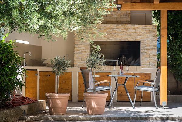 Outdoor patio with stone grill, kitchenette, and olive trees.