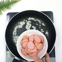 Bắc chảo lên bếp, cho vào 2 muỗng canh dầu ăn, phi thơm 15gr hành tây, sau đó cho xúc xích (cắt lát) vào xào 2 phút. Kế tiếp cho rau củ vào, nêm gia vị với 1 muỗng canh đường, 1 muỗng canh hạt nêm, 1 muỗng canh ớt sa tế và 1 muỗng canh nước tương, xào rau củ trên lửa lớn khoảng 2 phút.