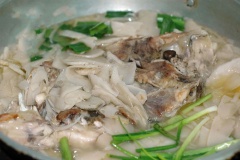 Chờ khi nước thật sôi thì mới cho cá vào, tiếp tục vặn nhỏ lửa đun thêm 20-30 phút nữa. Hành lá, ngò gai rửa sạch, cắt khúc.