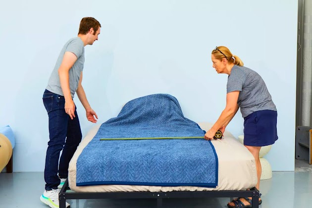 Een persoon die de Chappywrap Harborview Herringbone Navy Family-Size Blanket op een bed afmeet