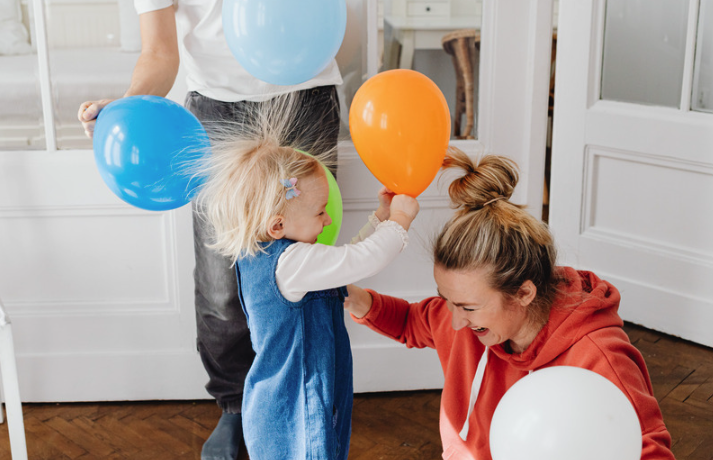 A toddler playing with balloons with a parent