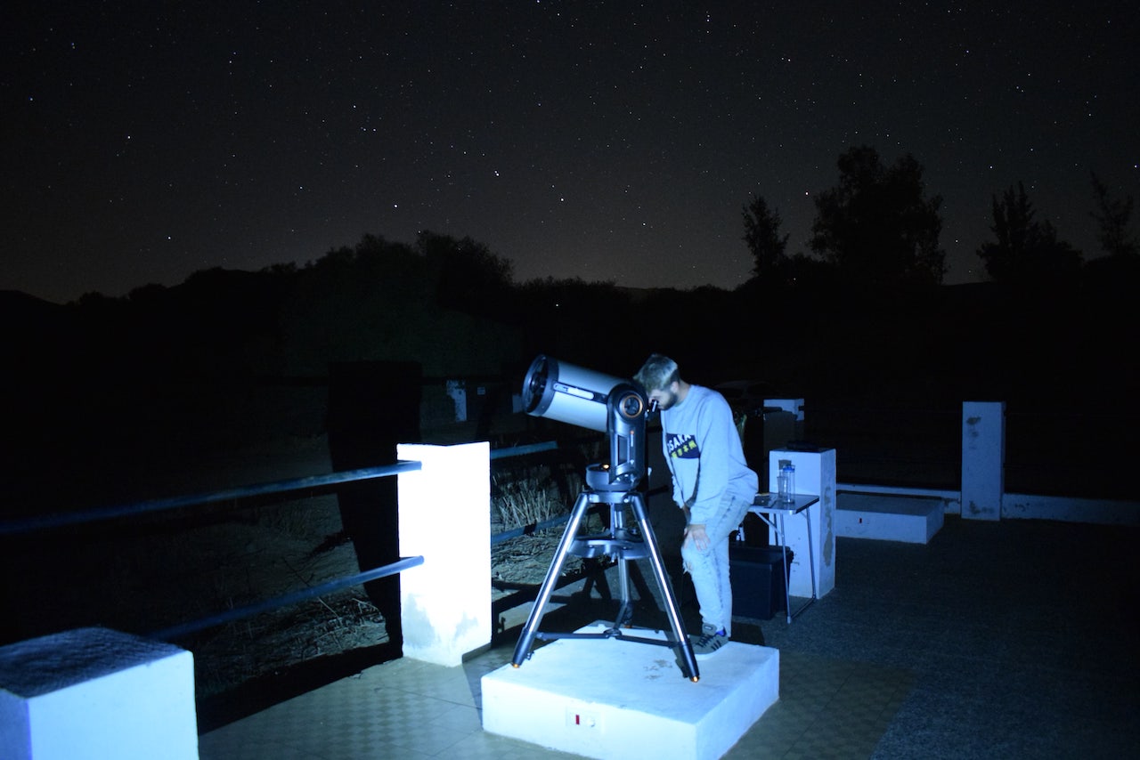 Visitor looking through a telescope during a nighttime astronomy activity in Alájar, with the Sierra silhouetted behind them.