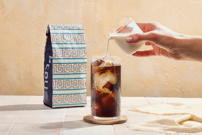 Cold brew coffee being poured over ice in a sunlit kitchen