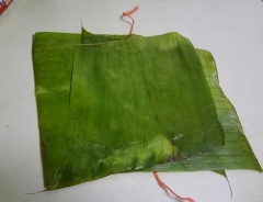 Để một sợi dây ở chín giữa, xếp một lớp lá chuối ngang, một lớp lá chuối dọc. Cho một phần tàu hũ ky vào chín giữa, túm hai mé lá lại với nhau, gấp xuống rồi bẻ gấp thêm lần nữa (gói lại như gói bánh tét), kéo dây cột sơ lại.
