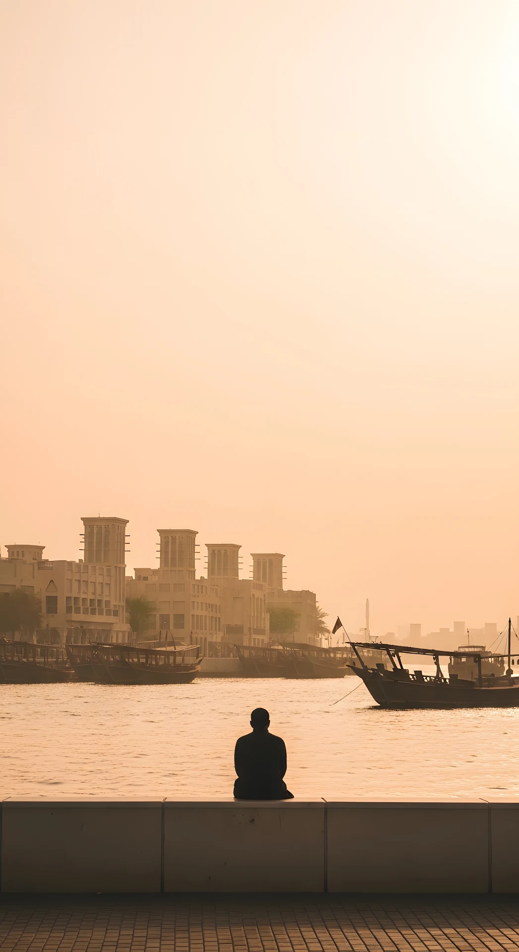 Hazy Golden Hour View of a Man Sitting by Dubai Creek and Historic Buildings - Free 4K mobile Wallpaper
