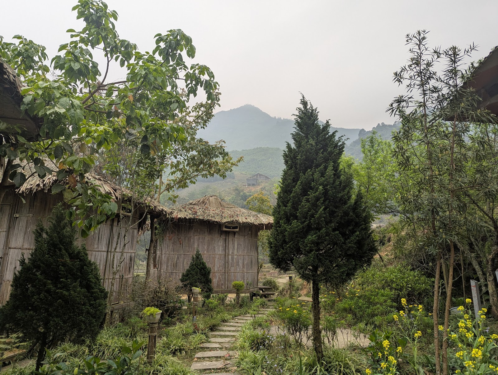 A photo of a couple small bamboo-walled constructions with dried straw
                 roofs. In the background are some mountains fading to blue.