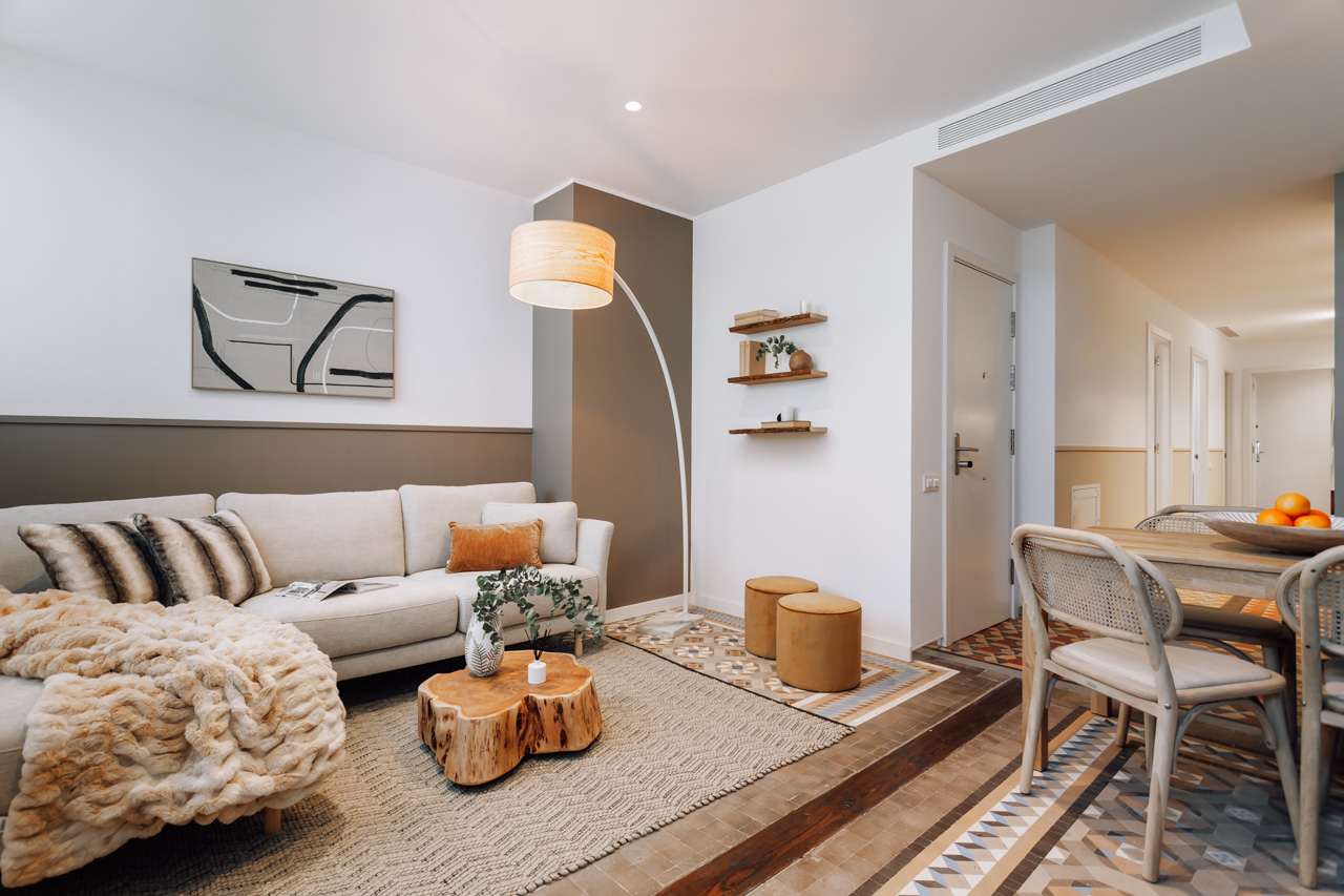 Plano general del salón, y parte del comedor y la cocina, con un gran sofá en forma de L y una mesa de madera maciza creada a partir de un tronco de árbol.