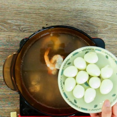 Khi nước dùng sôi, nêm 2 muỗng cà phê hạt nêm, 2 muỗng cà phê muối, 2 muỗng cà phê đường rồi cho tiếp 200gr huyết, 200gr tôm làm sạch, 10 quả trứng cút luộc đã bóc vỏ, khuấy đều tay.