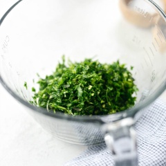 Chuẩn bị nguyên liệu. Tỏi bóc vỏ. Hành lá, ngò tây, ngò rí, lá oregano rửa sạch, lấy phần lá. Hành lá cắt khúc. Cho ngò tây, ngò rí, hành lá, lá oregano, tỏi vào máy xay thực phẩm xay sơ. Trút ra một tô riêng.