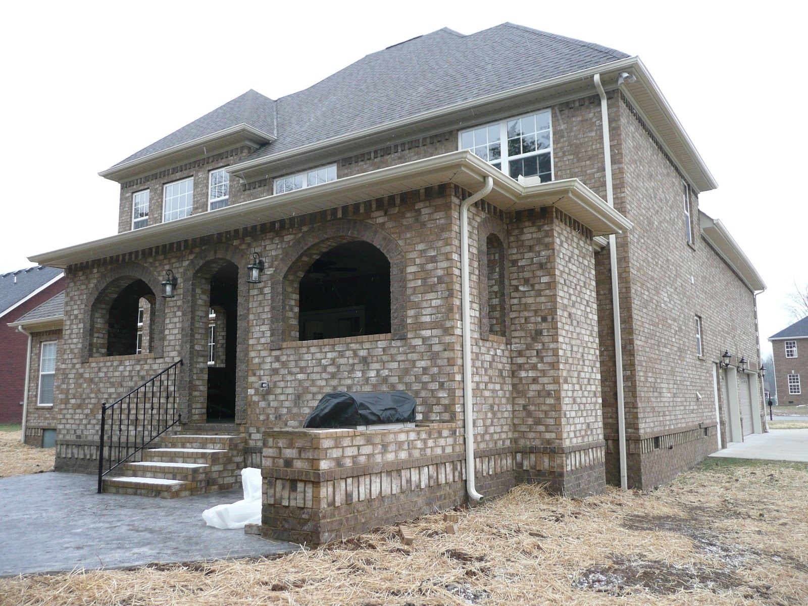 Exterior side view of a brick house featuring arched porch openings, a concrete patio, and steps with a metal railing.