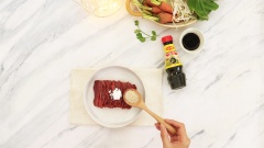 Dùng 200gr thịt bò thái lát mỏng, trộn đều với 1 muỗng canh Maggi nắp đỏ, 1/2 muỗng canh hạt nêm Maggi, 1 muỗng cà phê bột bắp rồi ướp trong 10 phút.