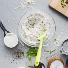 Cho bột mì, phô mai, bột nở, muối, baking soda, tiêu, hẹ băm vào tô rồi trộn đều. Cho kem chua vào và đảo đều. Cho sữa đông lạnh vào rồi trộn đều cho tới khi tất cả hòa quyện.