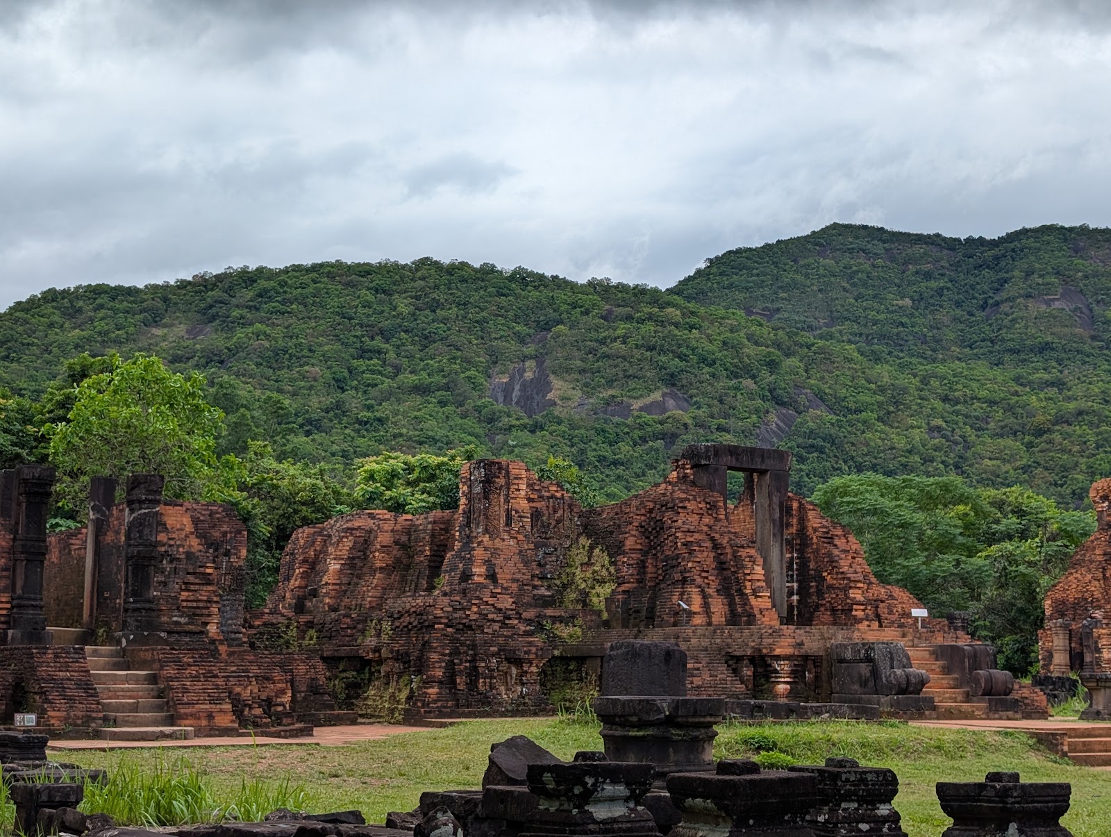 Photo of reddish brown temple ruins with lush green hills
                 in the background